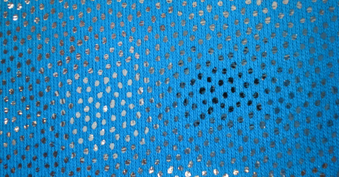 Blaue Strickware mit glänzenden silbernen Punkten, die mit Heißprägefolie und PERICOAT FL-Hotmelt hergestellt wurde.